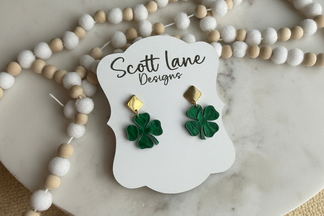 Pair of green shamrock earrings on a Scott Lane Designs card with decorative beads on a marble surface.