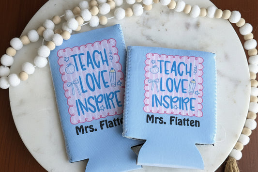 Two blue can coolers with personalized text on a marble surface.