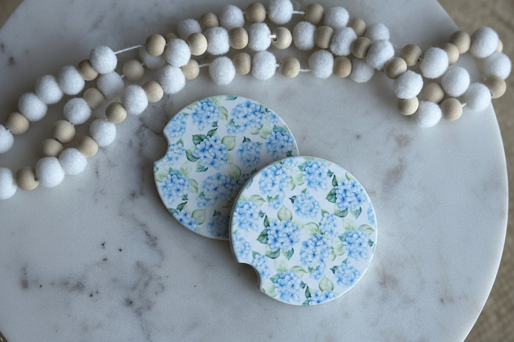 Two floral coasters on a marble surface with a string of beads.