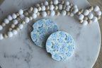 Two floral coasters on a marble surface with a string of beads.