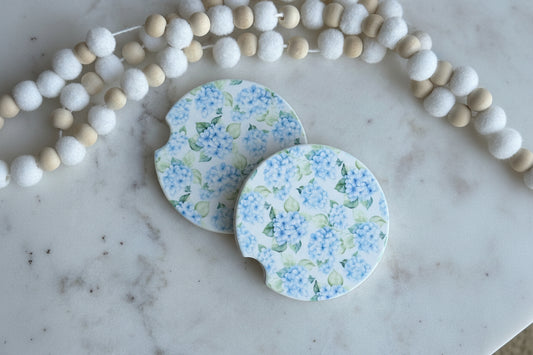 Two floral-patterned coasters on a marble surface with decorative beads.